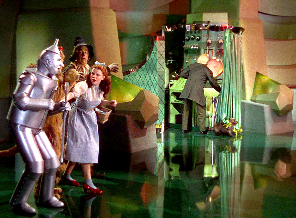 A still from the film "The Wizard of Oz", where Dorothy discovers the 'powerful' wizard is an old man hiding behind a curtain.