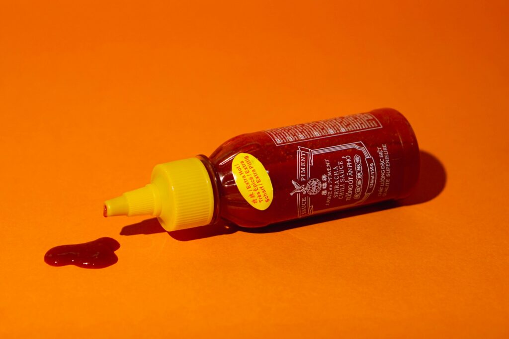 A bottle of red sauce on an orange backrgound. The bottle lies on its side with some sauce dripping out. Photo by frogses production on Unsplash