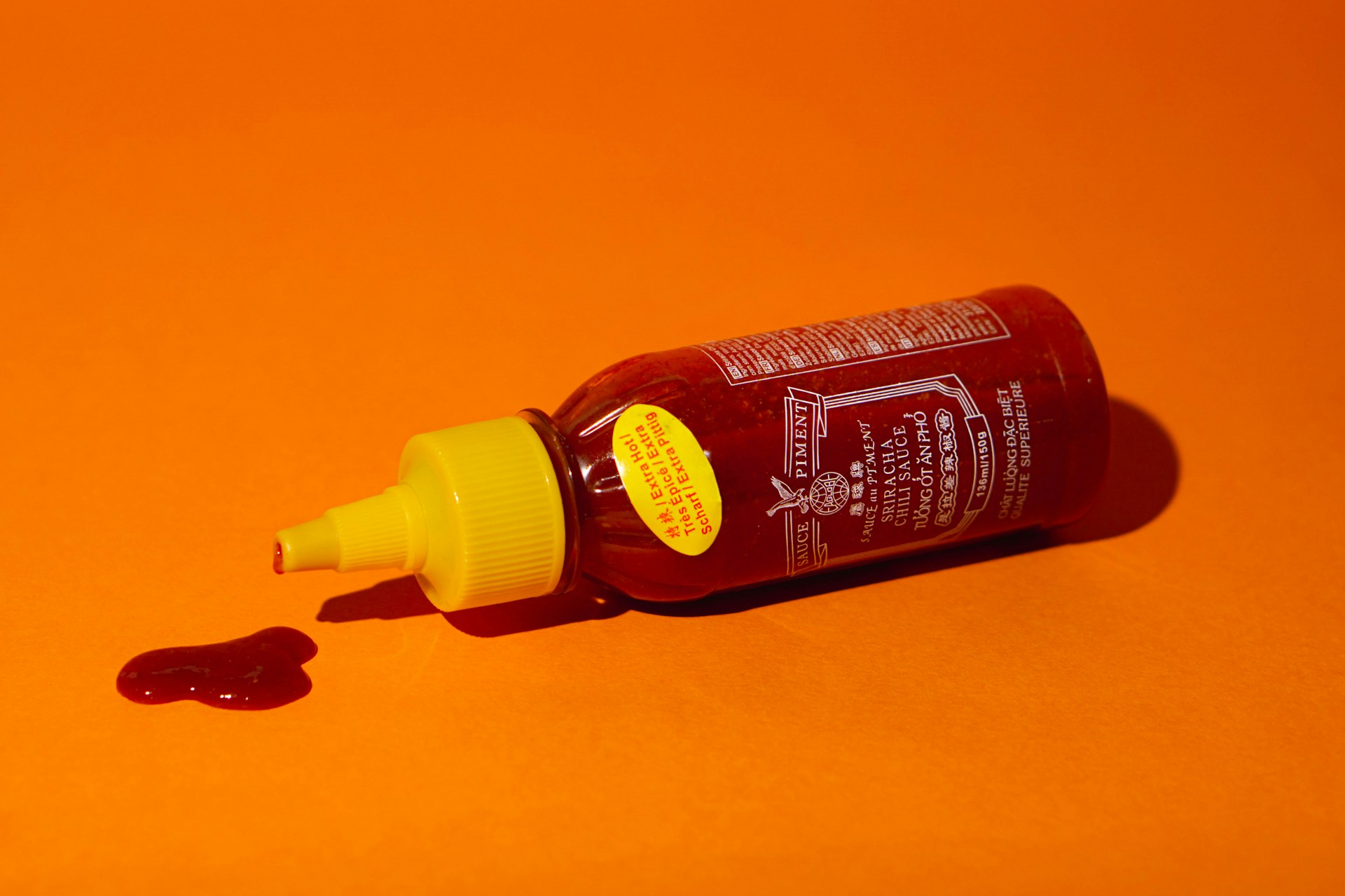 A bottle of red sauce on an orange backrgound. The bottle lies on its side with some sauce dripping out. Photo by frogses production on Unsplash